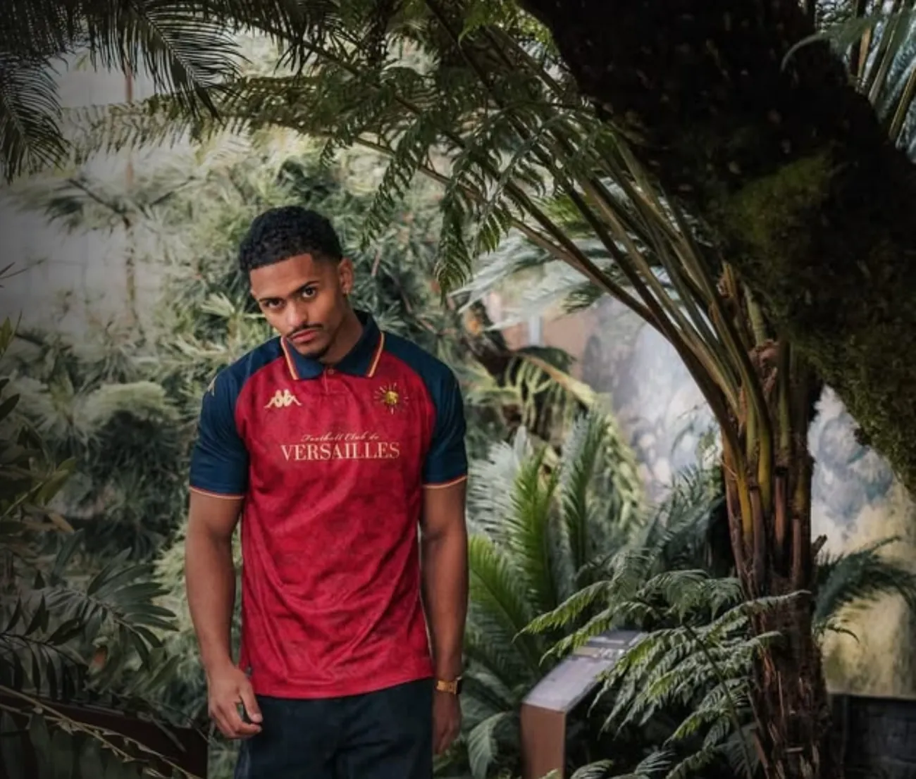 Modelo vestindo camisa de futebol vermelha e azul-marinho